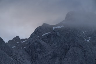 A dramatic view of towering peaks in the Bavarian Alps, partially covered by swirling mist The