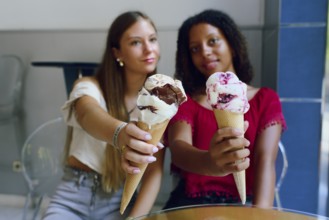 Two teenage friends, a Caucasian girl and an African girl, happily holding and showcasing their ice