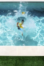 A young boy in a yellow shirt and blue shorts jumps energetically into a bright blue swimming pool,