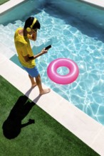 A person in vibrant attire enjoys music with headphones at a pool. Next to them, a pool float adds