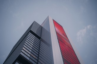Low-angle view of a modern skyscraper with a striking red facade against a clear sky. The sleek