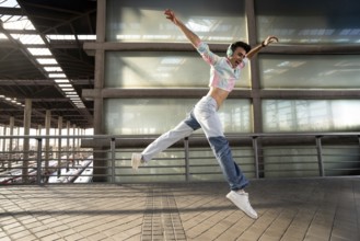 A young person in vibrant attire and headphones joyfully jumps in mid-air on an urban walkway, with