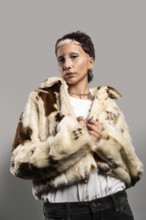 A woman with distinctive makeup and jewelry poses confidently in a stylish faux fur coat. The