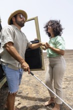 A blind man, assisted by a companion, steps out of a motorhome into an arid landscape, experiencing