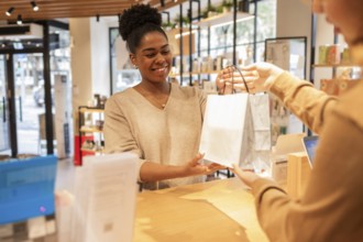 A customer service assistant in a bright cosmetics store smiles while handing a shopping bag to a