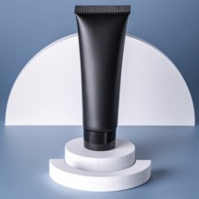 A sleek black cosmetic tube stands atop layered white circular podiums against a soft blue