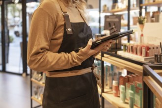 A worker in a cozy cosmetics store checks inventory using a tablet. The store is warmly lit, with