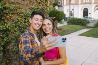 A joyful lesbian couple takes a selfie while enjoying a sunny day in a park. Their smiles reflect
