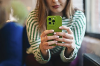 A cropped unrecognizable young woman checks her smartphone while enjoying a coffee break at a cafe.