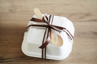 Elegantly packaged bento birthday cake in a white takeout box adorned with a chocolate-brown ribbon