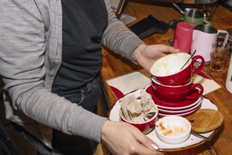 A person collects red cups with coffee grounds and plates on a wooden table in a coffee shop. This