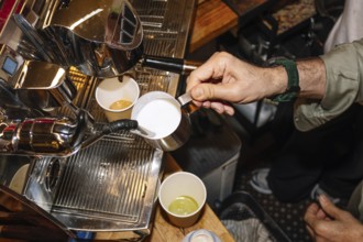 A skilled barista pours steamed milk from a metal pitcher into a cup of freshly brewed espresso,