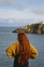 Back view of an unrecognizable woman with long red hair, standing at Cape Spear Lighthouse,