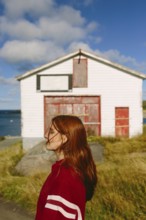 A young thoughtful woman with long red hair and eyes closed, wearing a red jacket, stands