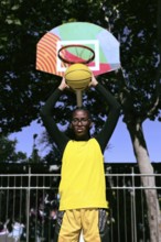 A black basketball player stands ready to shoot, holding a yellow basketball toward a vibrant,