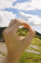 A creative shot capturing a distant hiker through an O-shaped hand frame against the lush, green
