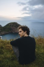 A young male sits serenely overlooking the calm waters from Signal Hill, St. John's. His relaxed