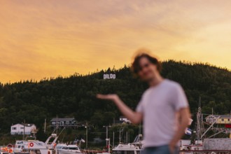 A young blurred Caucasian man playfully gestures towards the town sign DILDO in Dildo, Newfoundland
