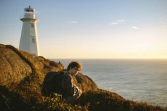 A young man relaxes near Cape Spear Lighthouse in Newfoundland, Canada, looking out towards the