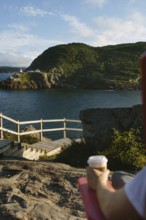 Cropped unrecognizable person sitting on rocks at Signal Hill, holding a coffee cup with a scenic