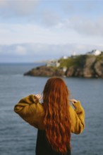 Back view of unrecognizable woman with long red hair, wearing a yellow sweater, overlooking a