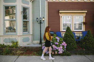 A young woman walks past charming houses with vividly painted facades in St John's, Newfoundland &