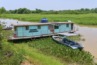 A houseboat parks on the riverbank next to a small boat surrounded by aquatic plants, Porto Jofre,