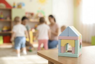 Pastel wooden building bricks toys and blurry playing children in background in children day care