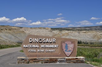 Dinosaur National Monument entrance sign with stone landscape in background under blue sky,