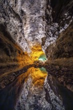 Lava tunnel, illuminated lava cave with perfect reflection in an underground lake, Cueva de los