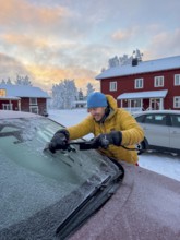 Young man scrapes off frozen car window, in the morning, Ranua, Lapland, Finland