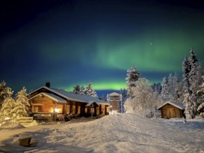 Northern lights, aurora borealis in the night sky, illuminated wooden house in snowy landscape,