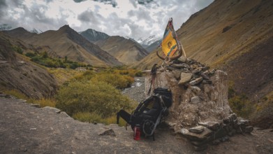 Large hiking backpack leaning at a stone place of worship and Buddhist prayer flag on a rocky