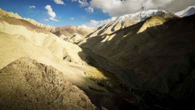 Dramatic mountain landscape with strong light and shadow in the valley, snow-capped mountains in