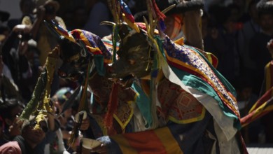People wearing colorful masks and costumes conduct an outdoor ceremony, traditional cultural