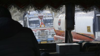 Two decorated trucks on a narrow road seen from the perspective of a vehicle, Manali-Leh Highway,