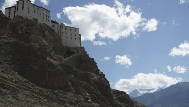 The Leh Palace is majestically perched high up on a rocky mountain with clouds in the bright blue