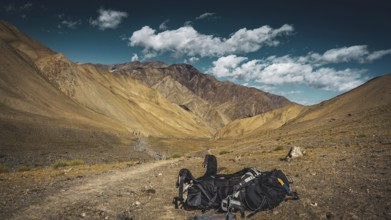 Hiking trail through a dry mountain landscape, a large backpack lying on the ground under a blue