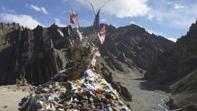 Traditional prayer flags on a stone hill in a wide mountain valley with a dry riverbed, trekking in