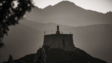 A monastery is majestically perched on a hill with mountains in the background at dusk, Leh,