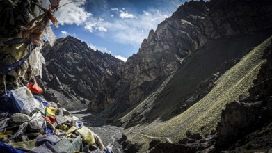 Mountain valley with prayer flags and dry riverbed surrounded by shady mountains, trekking in