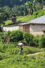 Local woman carrying luggage on her head, small village between green hills, on the edge of the