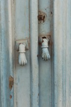Old decorative hand shaped door knockers on a traditional blue painted door on an house in the