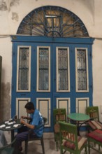 Tunis, Tunisia. 13th May 2024 A young Tunisian plays cards and drinks tea beside a traditional blue
