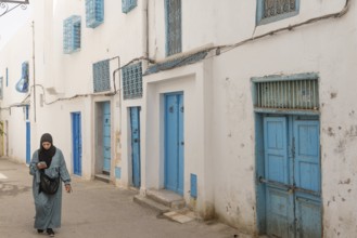 Tunis, Tunisia. 15th May 2024 A Tunisian Muslim woman using a cell phone walks past traditional