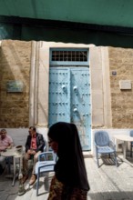 Tunis, Tunisia. 13th May 2024 An old wooden blue door with Tunisian men smoking shisha water pipes