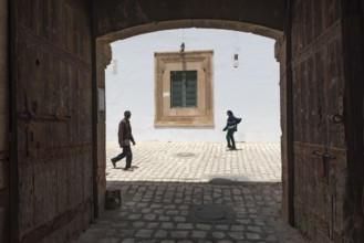 Tunisian men and women walk past some old wooden doors beside Bab Diwan the gate to Sfax Medina,