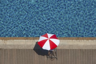 Bright red and white sunshade beside the deep blue water of a hotel pool in the summer time