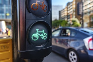 A green cycle lane traffic signal at a junction in a busy London city street with a car passing in