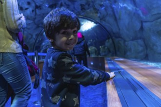 Young boy happily exploring an aquarium tunnel, discovering marine life and experiencing